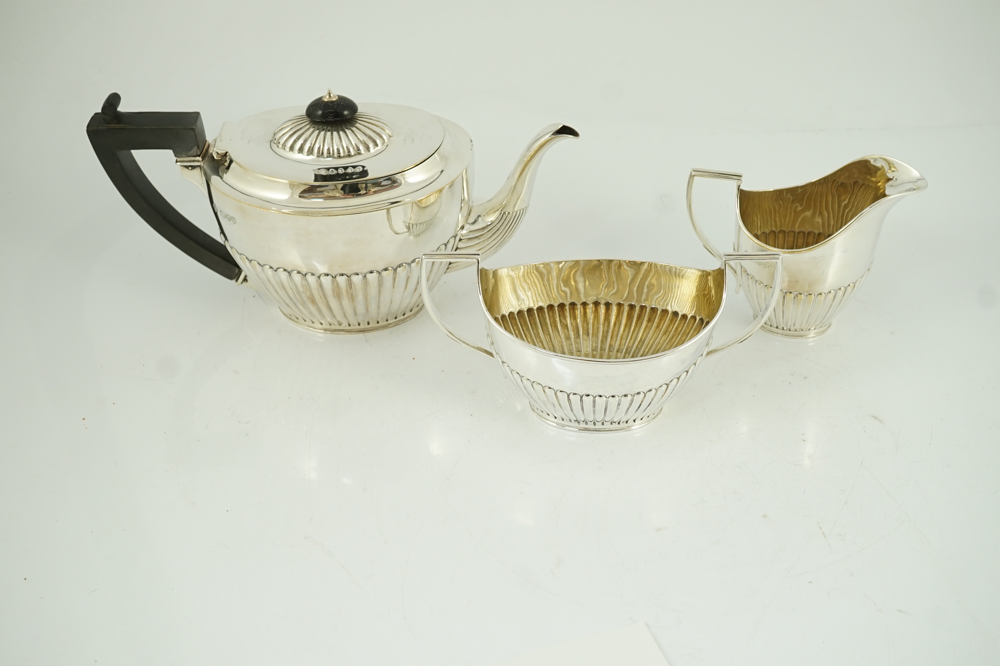 A late Victorian oak cased demi-fluted oval silver three piece tea set, by Martin, Hall & Co